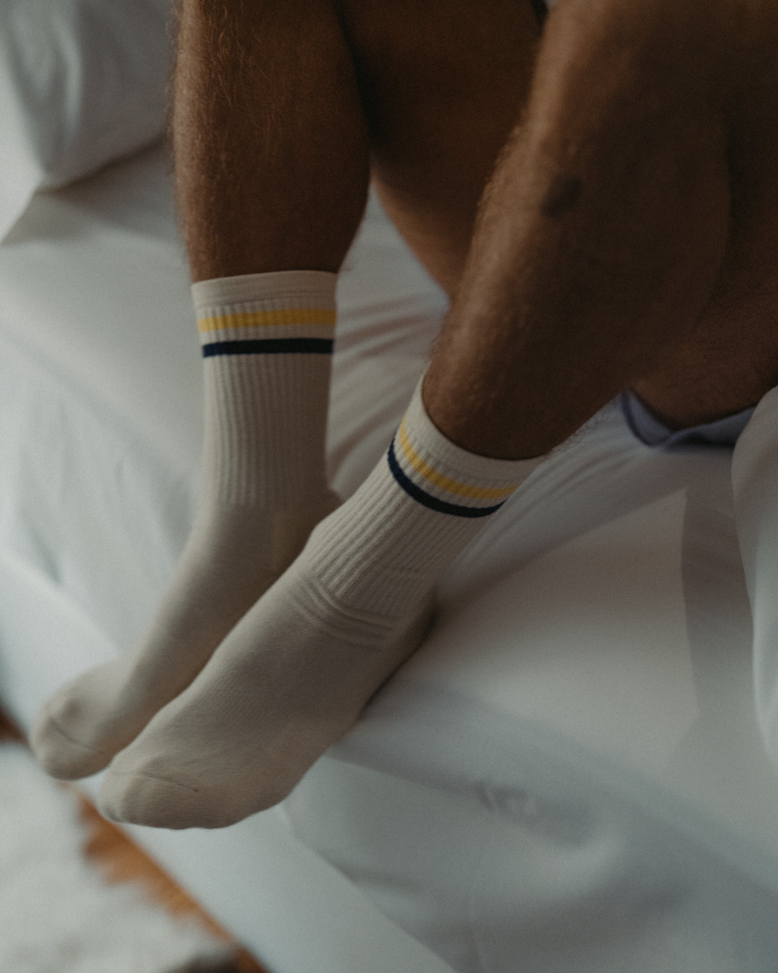 Person wearing white socks with yellow stripes sitting on a bed.