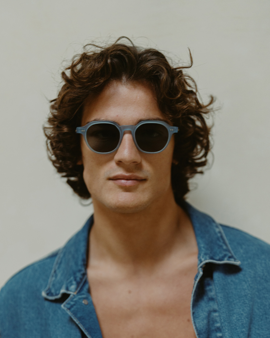 Man wearing sunglasses and a denim shirt against a plain background